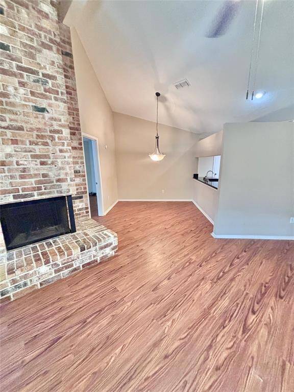 This inviting dining room features a high ceiling, a charming brick fireplace, and wood-look flooring. The open layout includes a dining area with pendant lighting and a view into the kitchen through a pass-through window. Perfect for cozy gatherings.