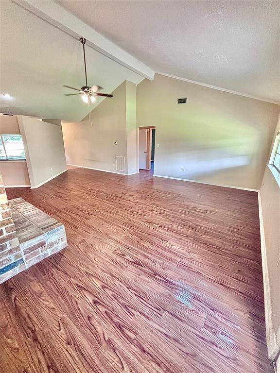 Spacious living area with high ceilings, wood flooring, and a ceiling fan. Large windows offer ample natural light. Cozy brick fireplace adds charm to this inviting space.