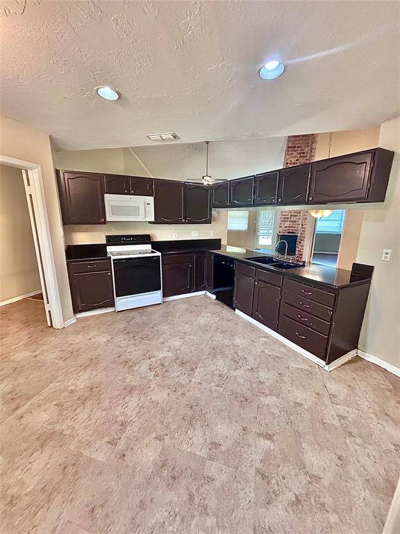 The kitchen features dark wood cabinets, a white stove and microwave, and black countertops. The space is open to the dining and living area and has recessed lighting.