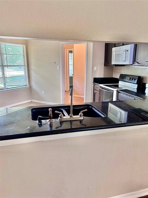 Modern kitchen with sleek black countertops, white appliances, and a central sink. Bright room with natural light from large windows.