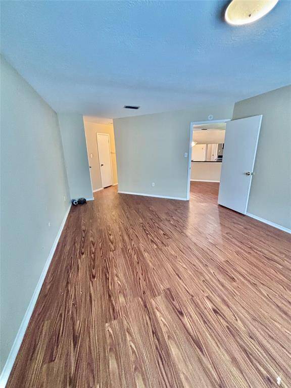 This photo shows a bright, primary bedroom with wood-look flooring and neutral walls. The room is connected to the ensuite vanity and bathroom, providing a spacious and open feel.