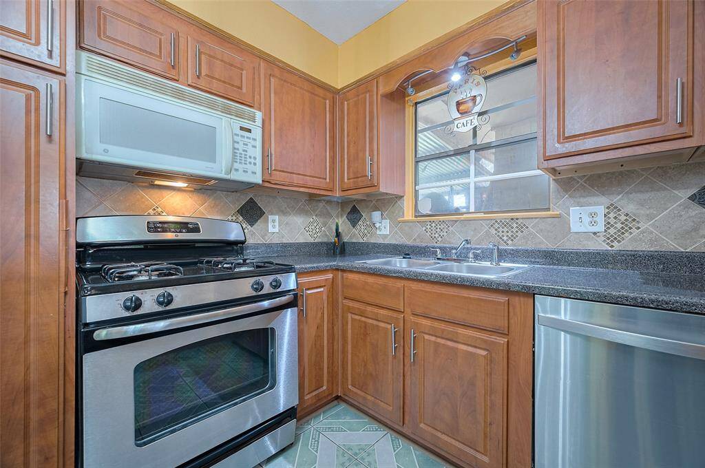 The kitchen is equipped with a GE gas range, a built-in microwave with a light and vent hood above the oven, and divided stainless steel sinks for easy cleanup. A Whirlpool stainless steel dishwasher, like new and rarely used (the owner still enjoys washing dishes by hand), adds a modern touch to the space.