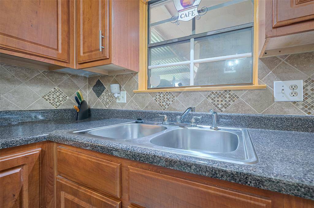 The kitchen boasts laminate countertops that mimic the elegance of granite, paired with a charming tile backsplash. Double divided stainless steel sinks with a faucet and vegetable sprayer make meal prep a breeze. A window above the sink looks out to the covered patio and backyard, offering a peaceful view while you cook.