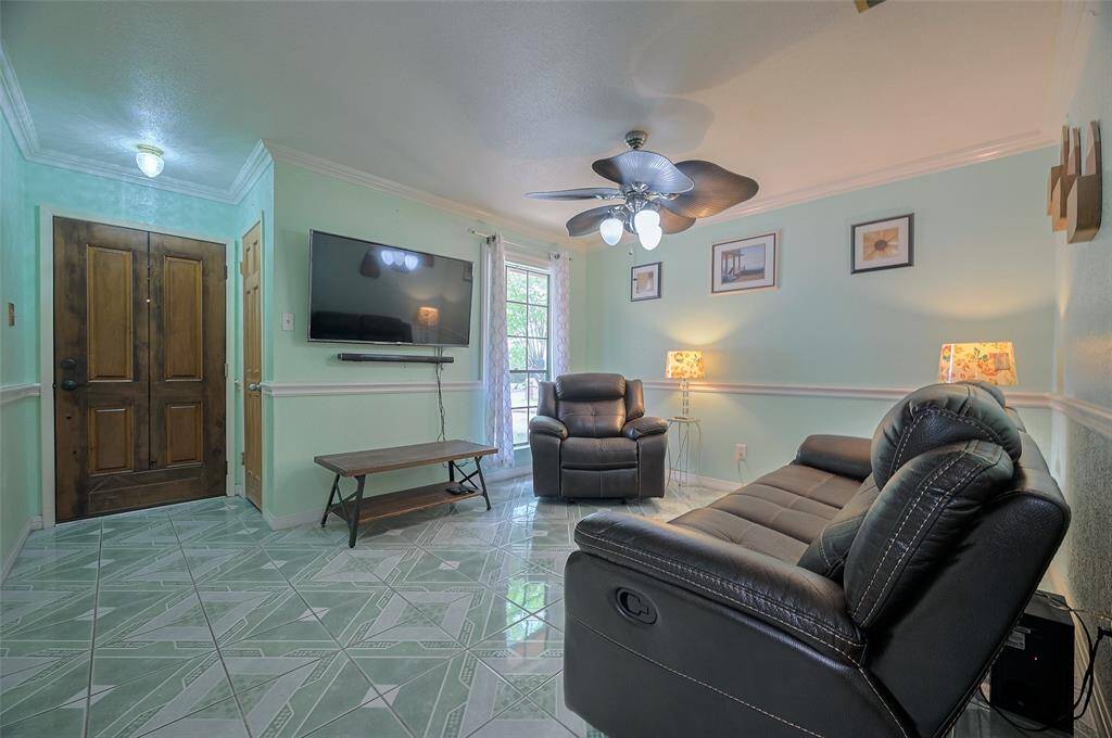 The foyer opens into a welcoming living room, highlighted by crown molding, chair-rail detailing, and a 5-blade ceiling fan for year-round comfort. A large front-facing window invites in beautiful natural light. Continuous tile flooring runs throughout the home — no carpet, easy to maintain and enjoy!