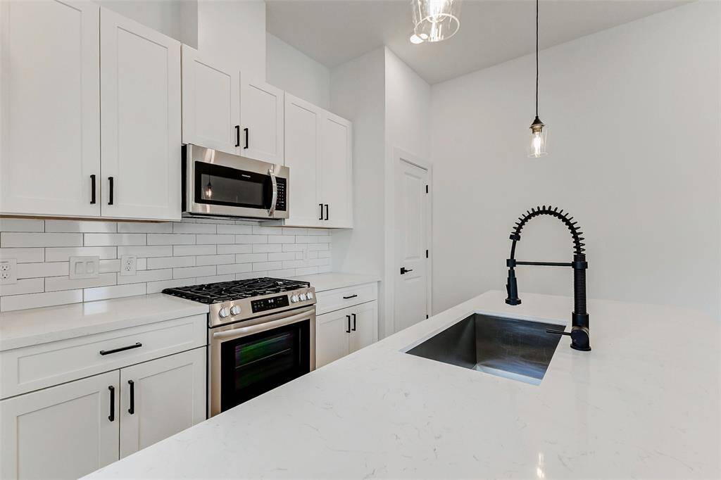 Modern kitchen with sleek white cabinetry, stainless steel appliances, and a stylish faucet. The subway tile backsplash and quartz countertops add a clean, contemporary touch.
