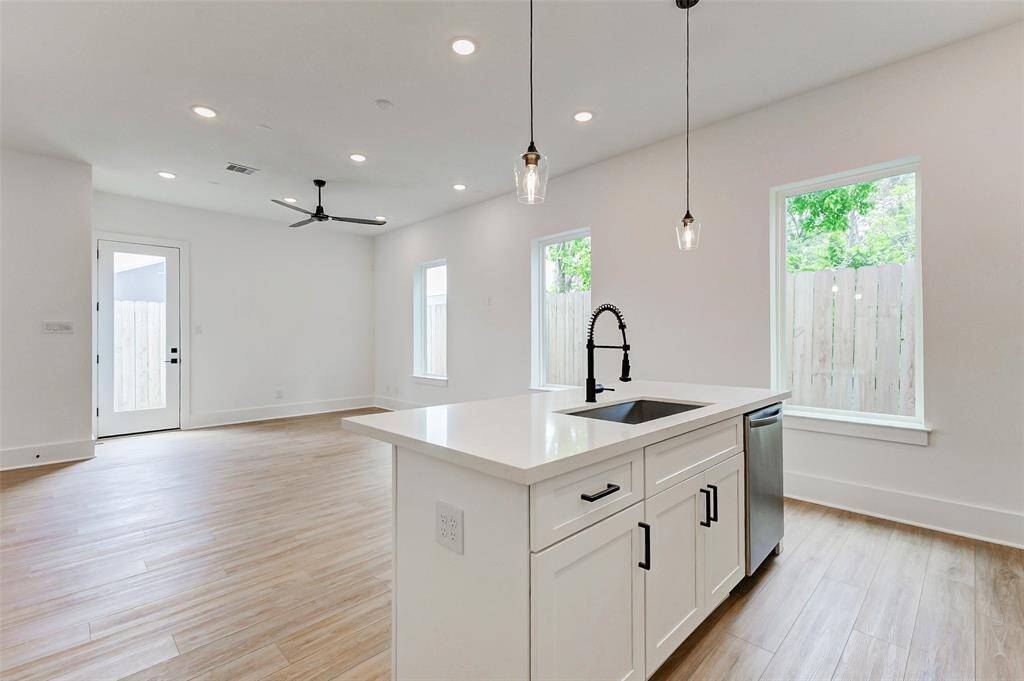 The kitchen features a sleek island with a sink, pendant lighting, and a contemporary faucet. Large windows and a glass door provide views of a fenced backyard.