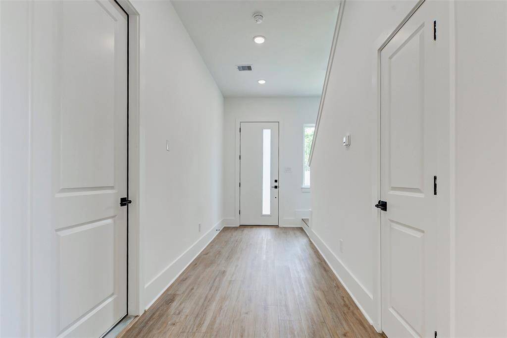 Bright and inviting entryway with sleek floors, modern white doors, and ample natural light from a window near the front door.