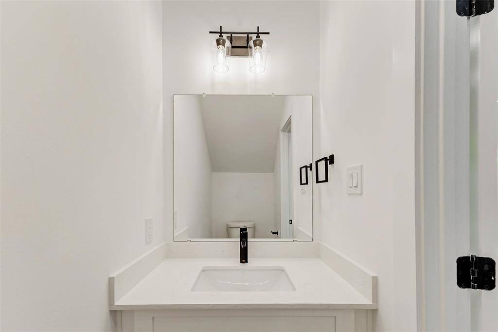 This is a modern half bathroom with a minimalist design, featuring a white countertop, a rectangular mirror, and stylish light fixtures. The clean lines and neutral tones create a fresh and inviting space.