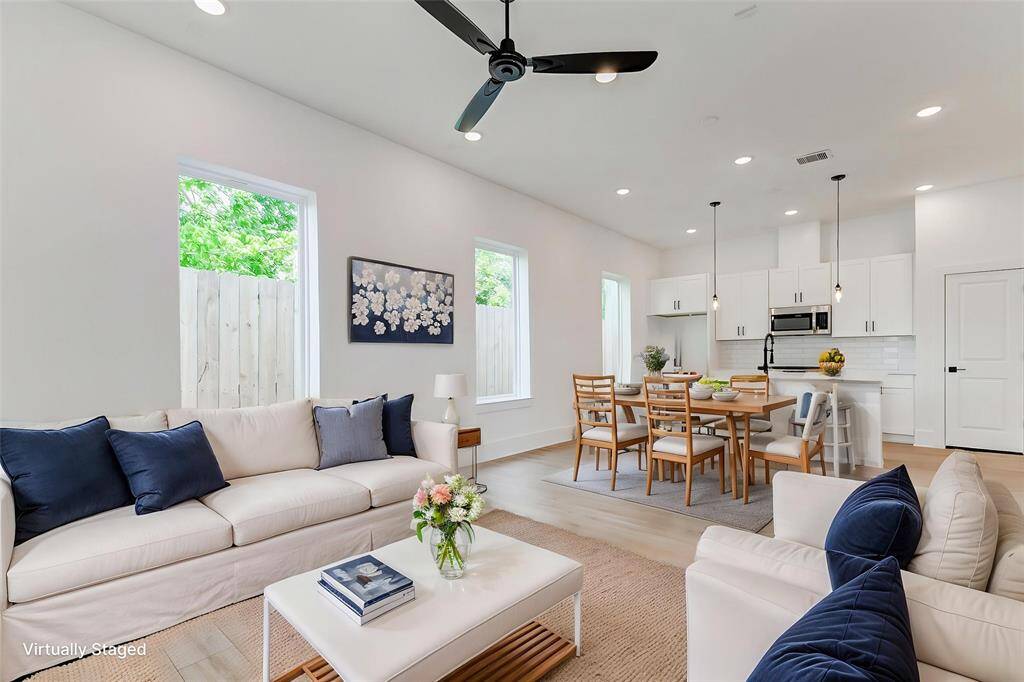 Bright, open-concept living and dining area with modern furnishings. The space features large windows, a ceiling fan, and a stylish kitchen with white cabinets and a breakfast bar. Perfect for comfortable and contemporary living.