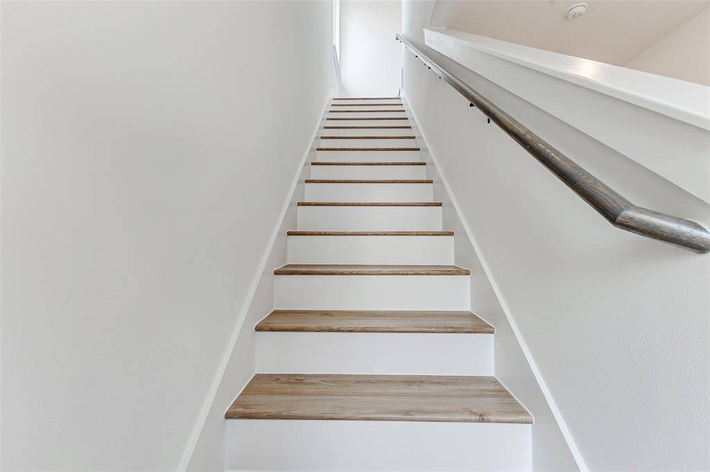 A modern staircase with light wood steps and a sleek, dark handrail. The walls are painted white, creating a bright and open feel.
