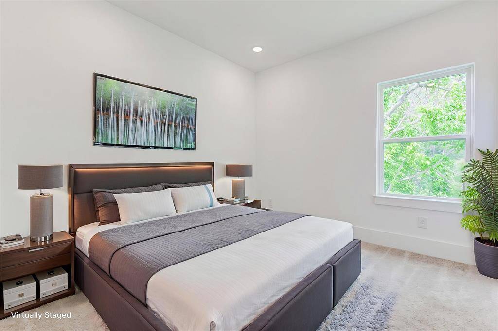 This is a virtually staged, bright bedroom featuring a modern aesthetic and a window providing natural light and a view of greenery.