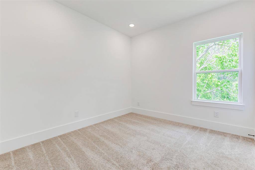 This room features clean white walls, plush carpet flooring, and a large window offering a view of greenery, creating a bright and inviting space.