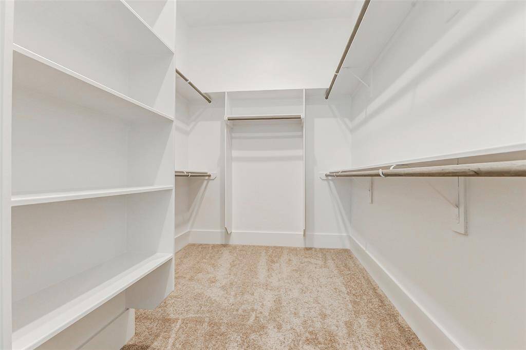 Spacious walk-in closet with ample shelving and hanging space, featuring clean white walls and soft carpet flooring. Ideal for organizing clothing and accessories.