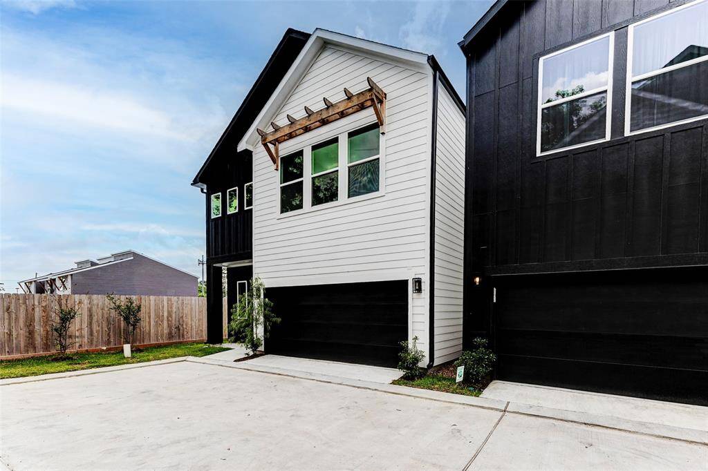 Modern two-story home with a sleek black and white exterior, featuring a front-facing garage and a small landscaped area. The property is adjacent to a wooden fence, providing a sense of privacy.