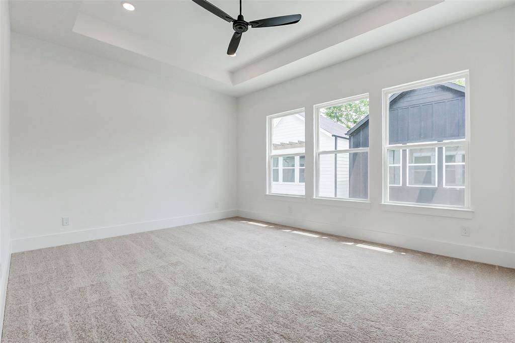 This bright, spacious room features large windows, neutral carpeting, and a modern ceiling fan, creating a welcoming and airy atmosphere.