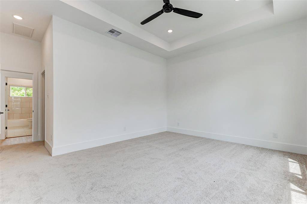 This spacious bedroom features a neutral color palette with plush carpeting and a ceiling fan. It opens to a well-lit bathroom, creating a seamless transition between spaces.