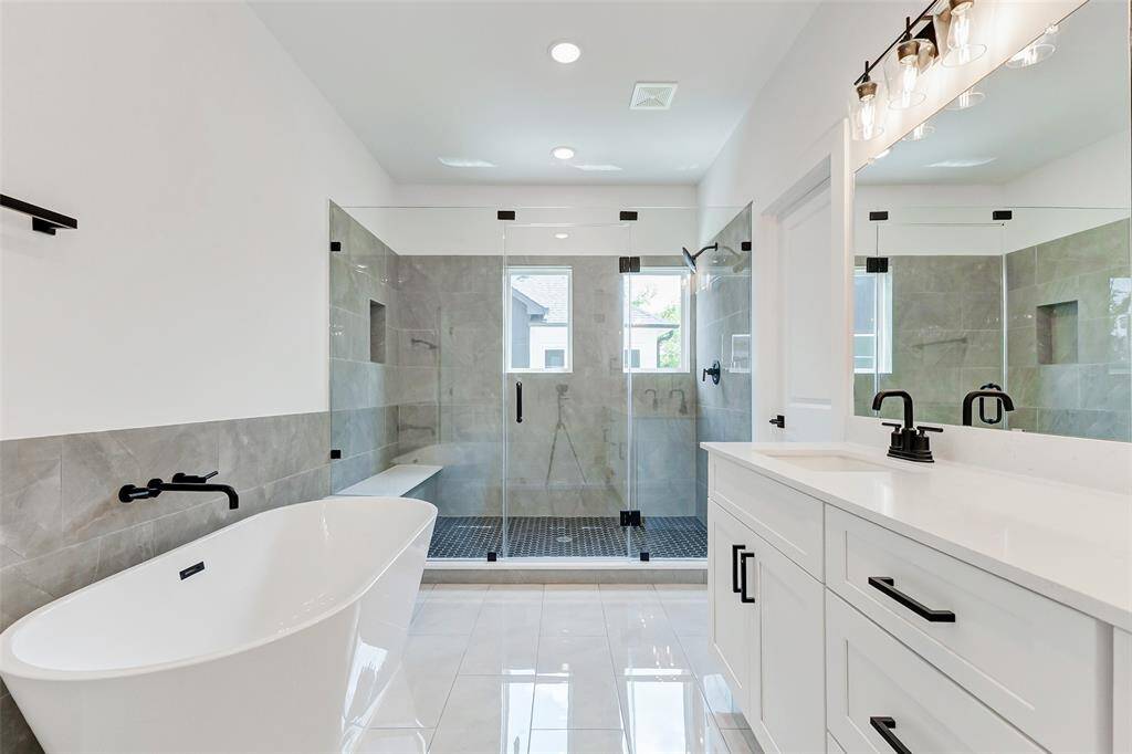Modern bathroom features a sleek freestanding tub, a large glass-enclosed shower, dual sinks with black fixtures, and elegant tile flooring, offering a luxurious and contemporary feel.