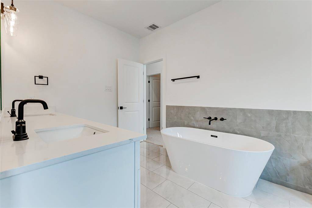 Experience luxury in this bathroom with a modern freestanding tub, dual sinks with sleek black faucets, and pristine white finishes throughout.