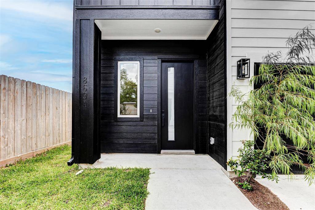 Sleek black front door, vertical window, and dark wood siding. It's complemented by a small, neat garden and a wooden fence, offering a welcoming and contemporary look.