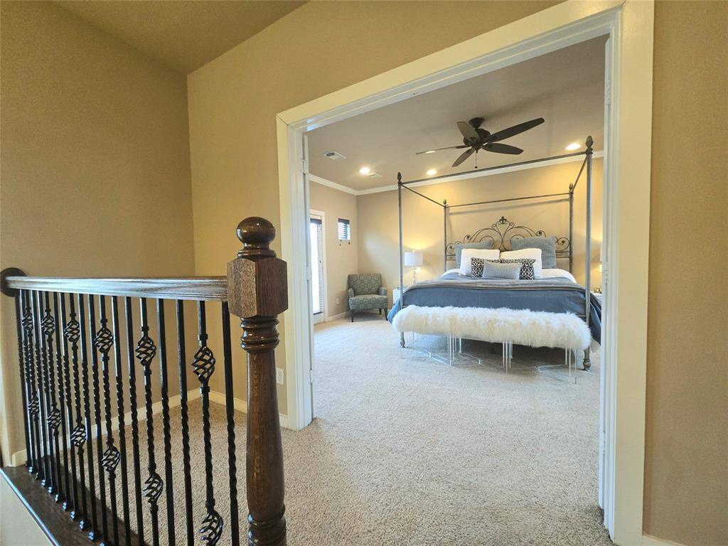 As you step back, the primary suite is revealed through wide double doors, framed by a striking wood and wrought iron banister, elevating the sophisticated ambiance of the space.