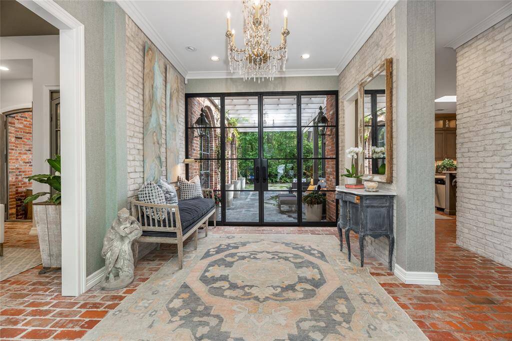 The inviting entryway features all-brick flooring, elegant chandelier, and glass door leading to a lush outdoor space.