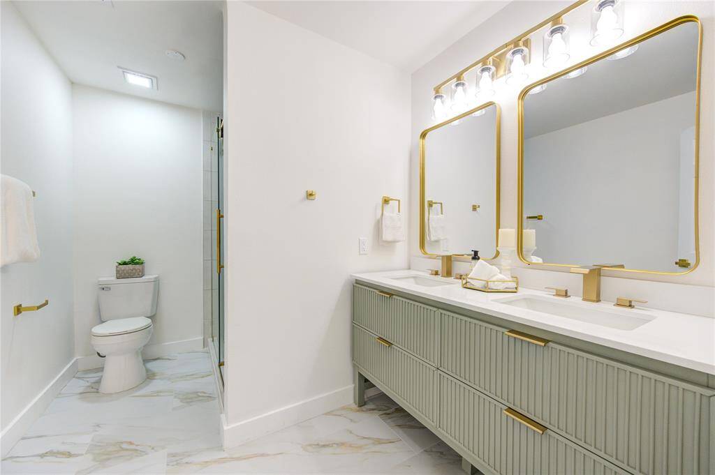The primary bathroom has been fully renovated with new tile floors, a walk-in shower with a modern glass door, and a double vanity with Quartz countertops. The sleek design and updated fixtures add a spa-like feel to the space.