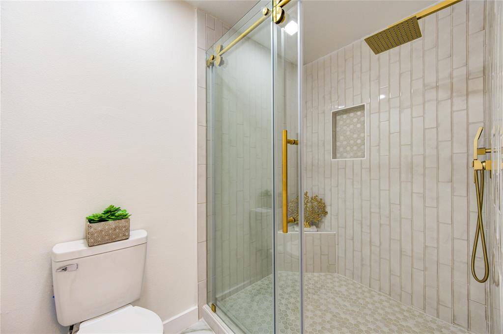 The primary bathroom features a luxurious walk-in shower, designed with modern elegance. The shower is equipped with a rain shower head, offering a spa-like experience with a gentle, soothing flow of water. The walls are beautifully finished with subway tile installed vertically, creating a sleek, contemporary look. The updated frameless glass door allows the design to shine, providing an open and airy feel.