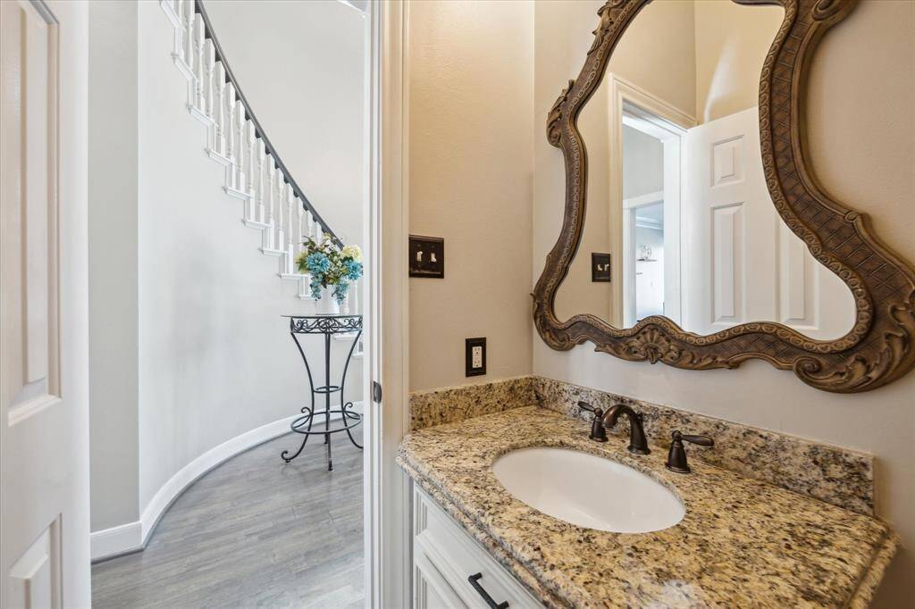 The downstairs powder room offers a stylish vanity with granite countertops, bronze finishes, and a framed mirror for a refined, functional guest space.