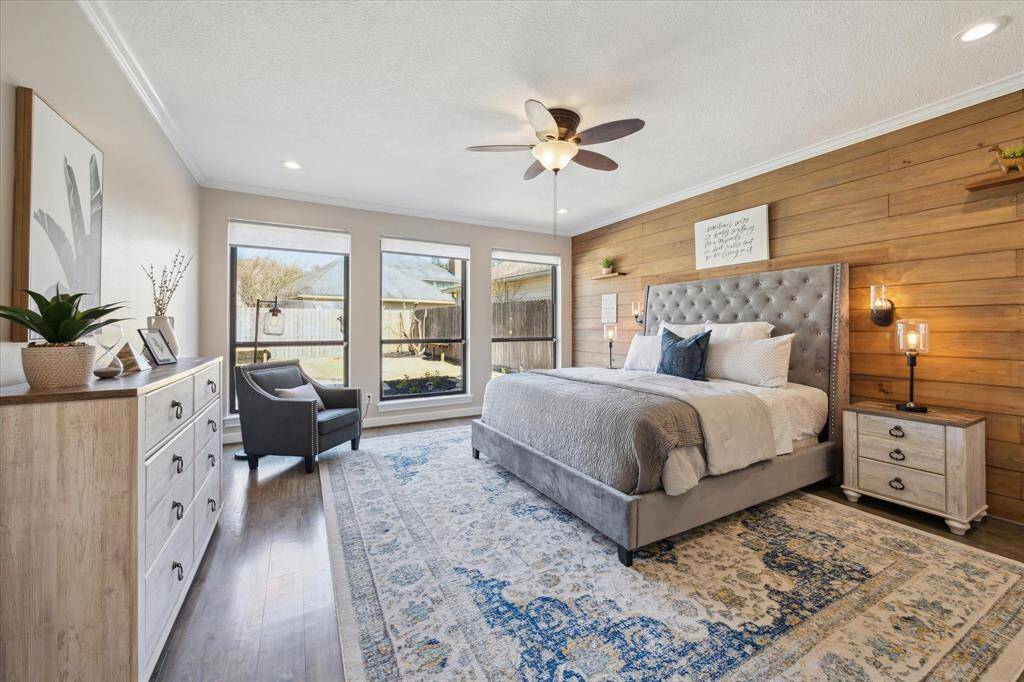 The remodeled first-floor primary suite is a private retreat with a custom shiplap accent wall, electric shades, wood floors, and a high ceiling with crown molding.