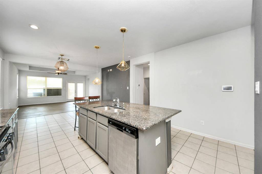 This photo showcases an open-concept kitchen and living area. The kitchen features a large island with granite countertops, stainless steel appliances, and modern pendant lighting. The space flows into a bright living area with large windows and tiled flooring.