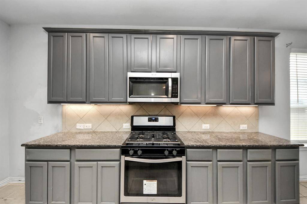 This kitchen features sleek gray cabinets, modern stainless steel appliances, and a spacious granite countertop, creating a stylish and functional cooking space.