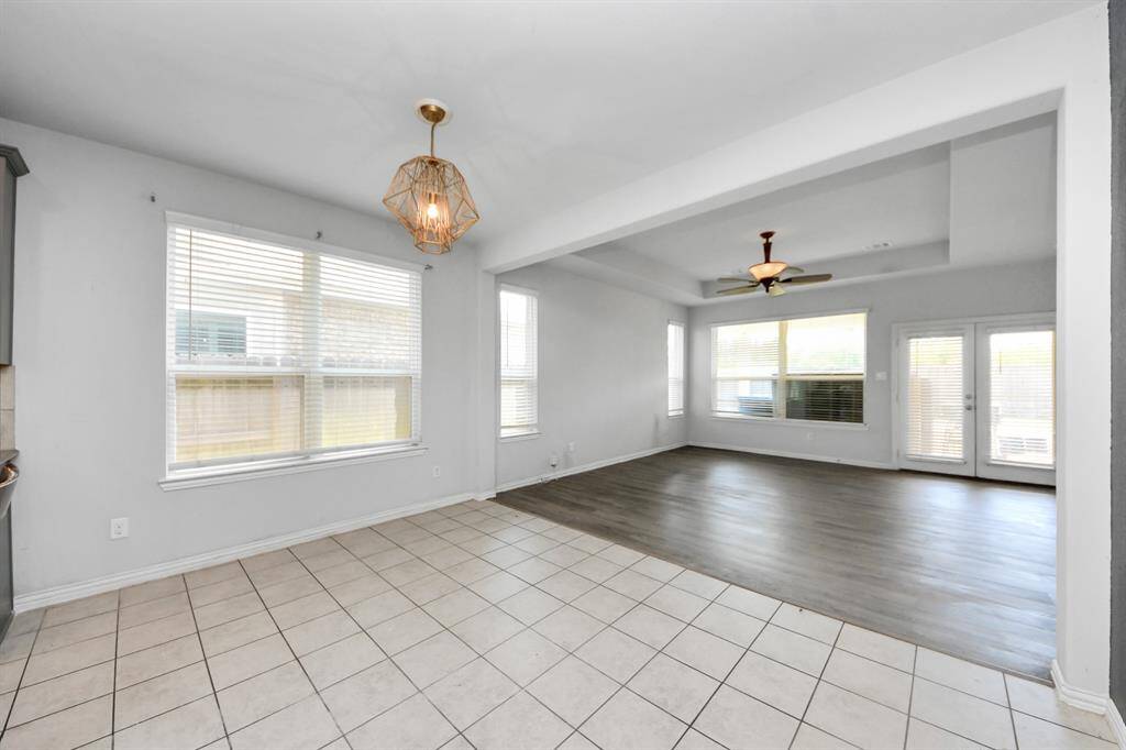 This photo showcases a bright, open-plan living and dining area with large windows, modern light fixtures, and a blend of tile and wood flooring. The space is airy and inviting, ideal for family gatherings and entertaining.