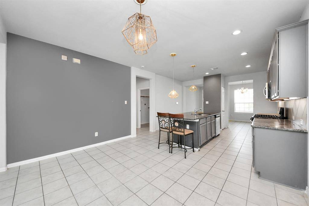 This photo showcases a modern kitchen and dining area with sleek gray cabinetry, a central island with seating, and stylish pendant lighting. The space features tiled flooring and ample natural light from a large window, creating a bright and inviting atmosphere.