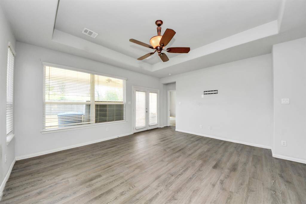 This bright living room features large windows, a ceiling fan, and wood flooring, opening to a patio through glass doors. Perfect for natural light and indoor-outdoor living.
