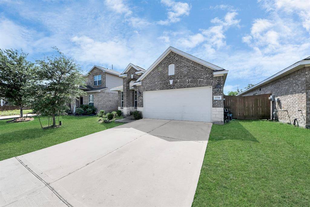This is a modern brick home with a spacious driveway leading to a two-car garage. It features a well-maintained front lawn and mature trees, set against a clear blue sky.