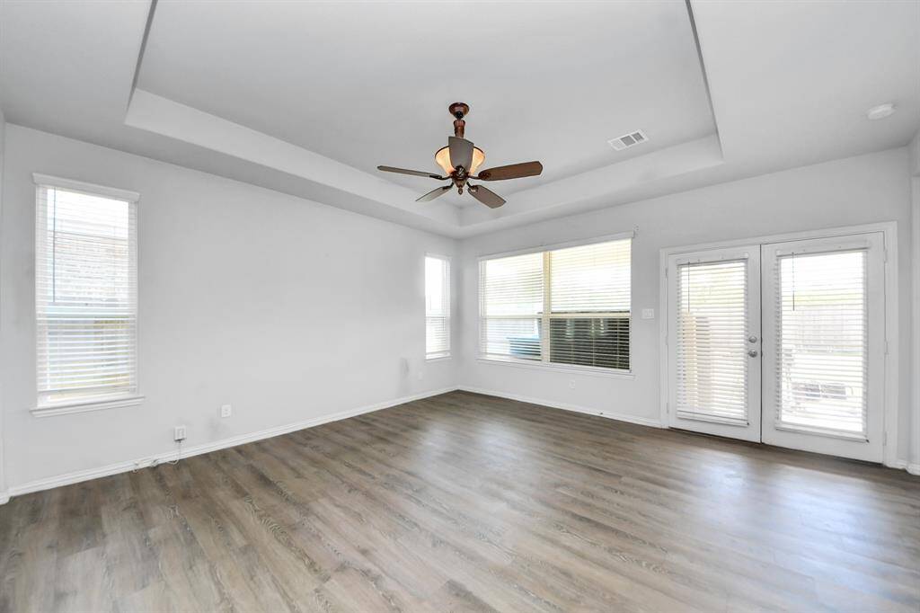This room features a large window with beige curtains, providing plenty of natural light. It has a unique recessed ceiling with a gold accent and a central light fixture. The walls are painted a soft gray, and the floor is carpeted, creating a cozy atmosphere.