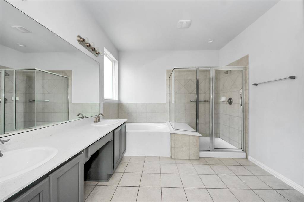 This spacious bathroom features a dual-sink vanity with ample counter space, a tiled shower, and a separate bathtub. It has a large mirror and plenty of natural light from a nearby window, creating a bright and inviting atmosphere.