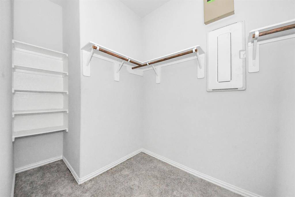 This photo shows a spacious walk-in closet with built-in shelving and hanging rods, offering ample storage space. The room is bright and has a clean, modern design.