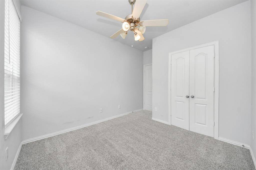 This room features soft gray walls and carpet, a ceiling fan with lights, a window for natural light, and double doors, ideal for a bedroom or office space.