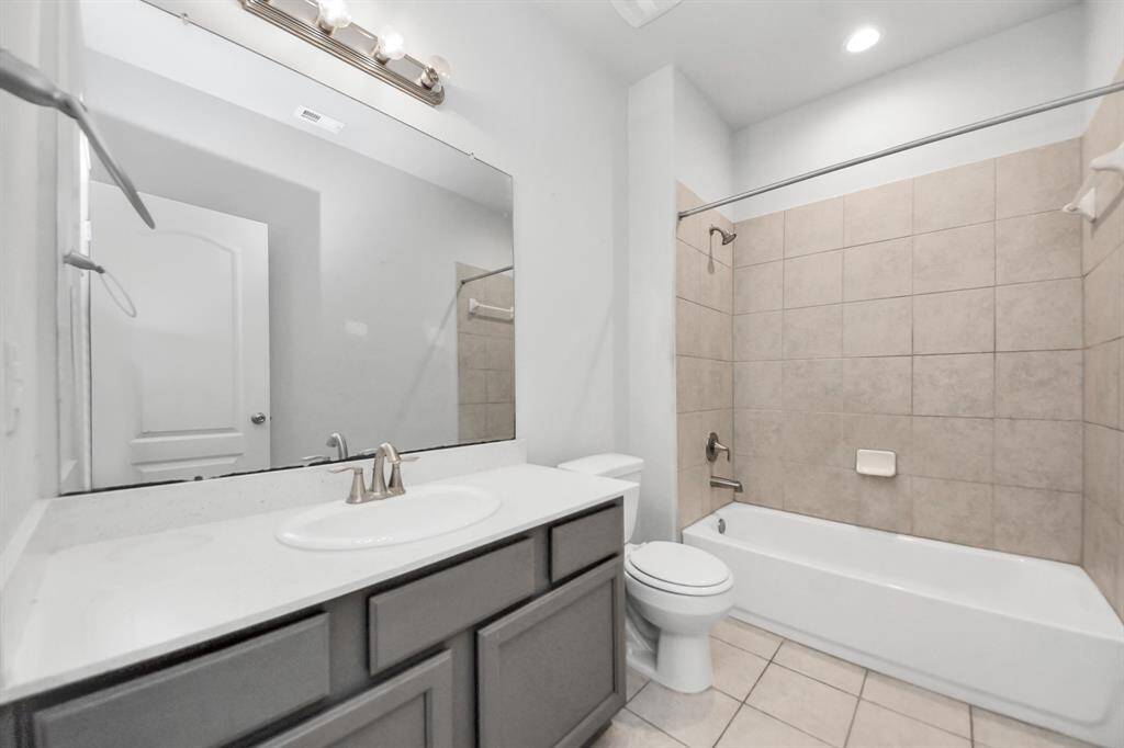 This bathroom features a modern design with a large mirror, a single-sink vanity, and neutral-colored tiles surrounding the bathtub and shower. The space is well-lit with overhead lighting and has a clean, bright appearance.