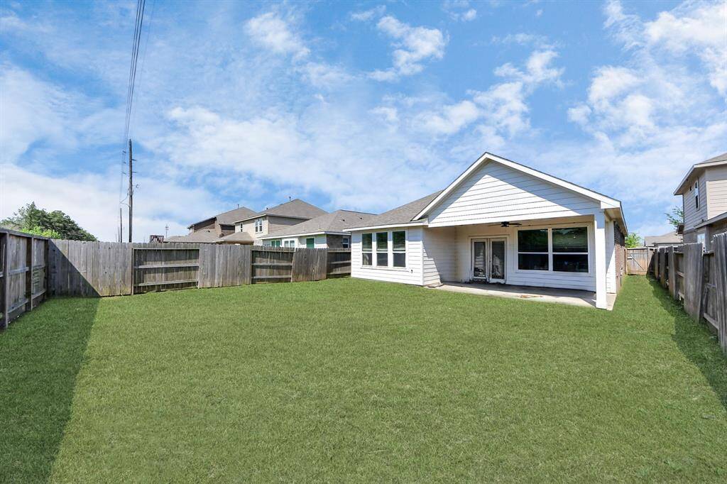This photo shows a spacious backyard with well-maintained grass, enclosed by wooden fencing. The house features a covered patio with large windows and a glass door, ideal for outdoor activities and relaxation.