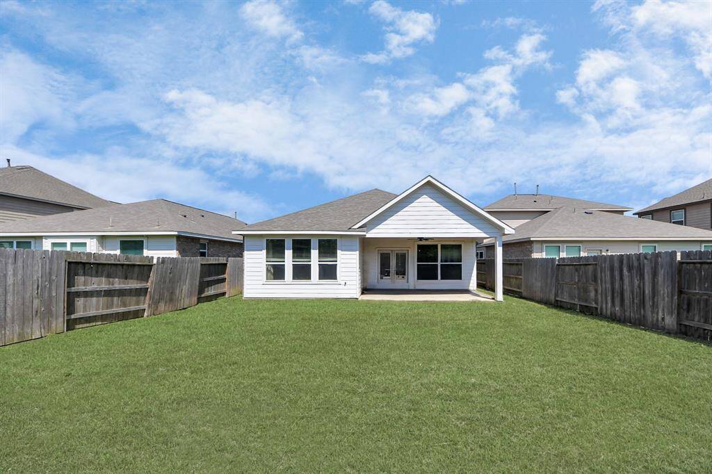 This photo showcases the backyard of a home with a well-maintained lawn, a covered patio, and wooden fencing for privacy. The exterior is modern with large windows, providing a bright and inviting atmosphere.