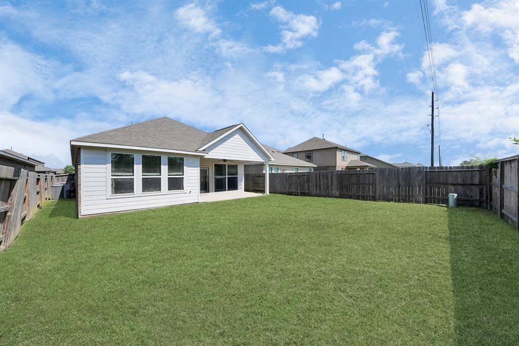 Spacious backyard with a well-maintained lawn, privacy fencing, and a view of a modern single-story house with large windows and a patio area. Ideal for outdoor activities and relaxation.