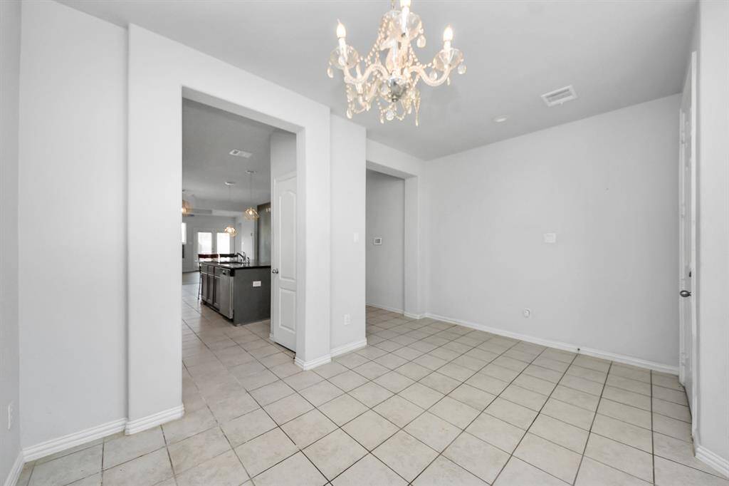 This photo showcases a bright, tiled entry area featuring a stylish chandelier. It opens up to a spacious kitchen with modern fixtures, providing a welcoming and elegant transition from the entrance to the main living space.