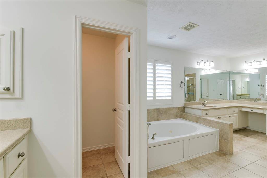 Large primary bath has double vanities, tile floors, private toilet closet and jacuzzi tub in view.