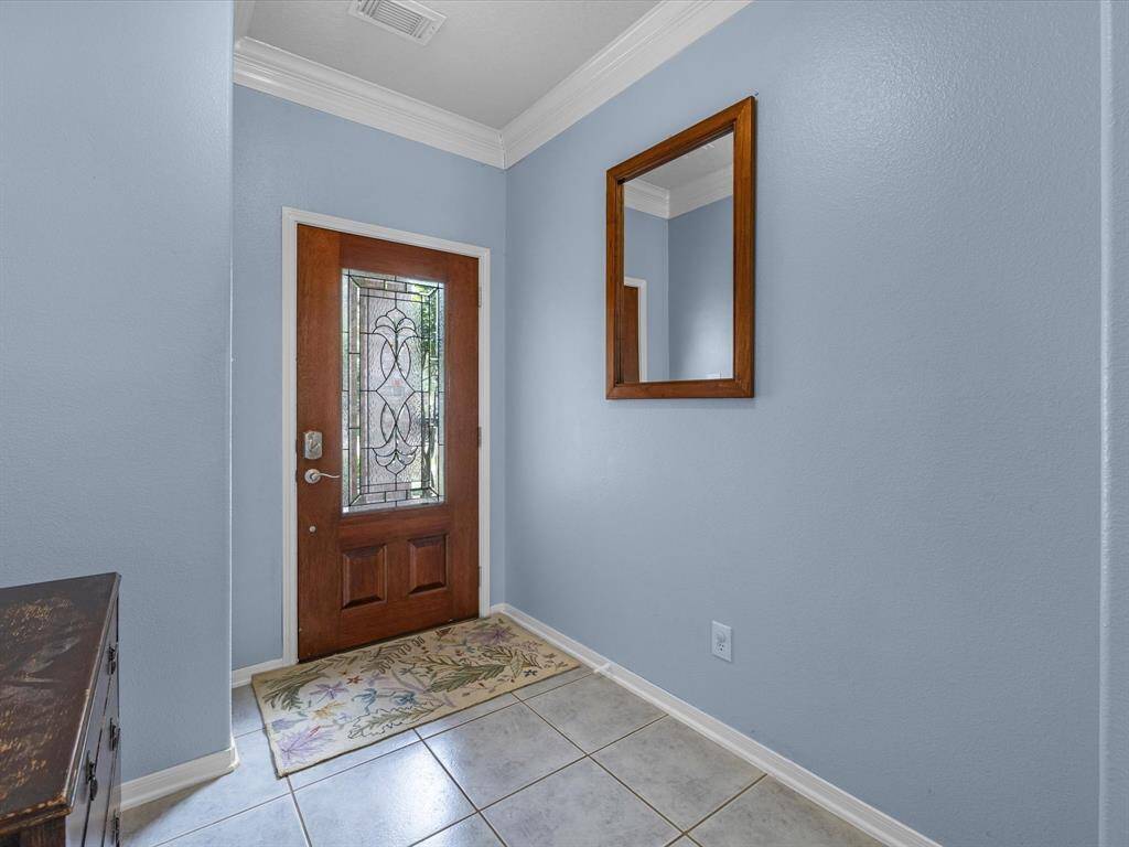 The large foyer entry has tile flooring and crown moulding with leaded glass front door.