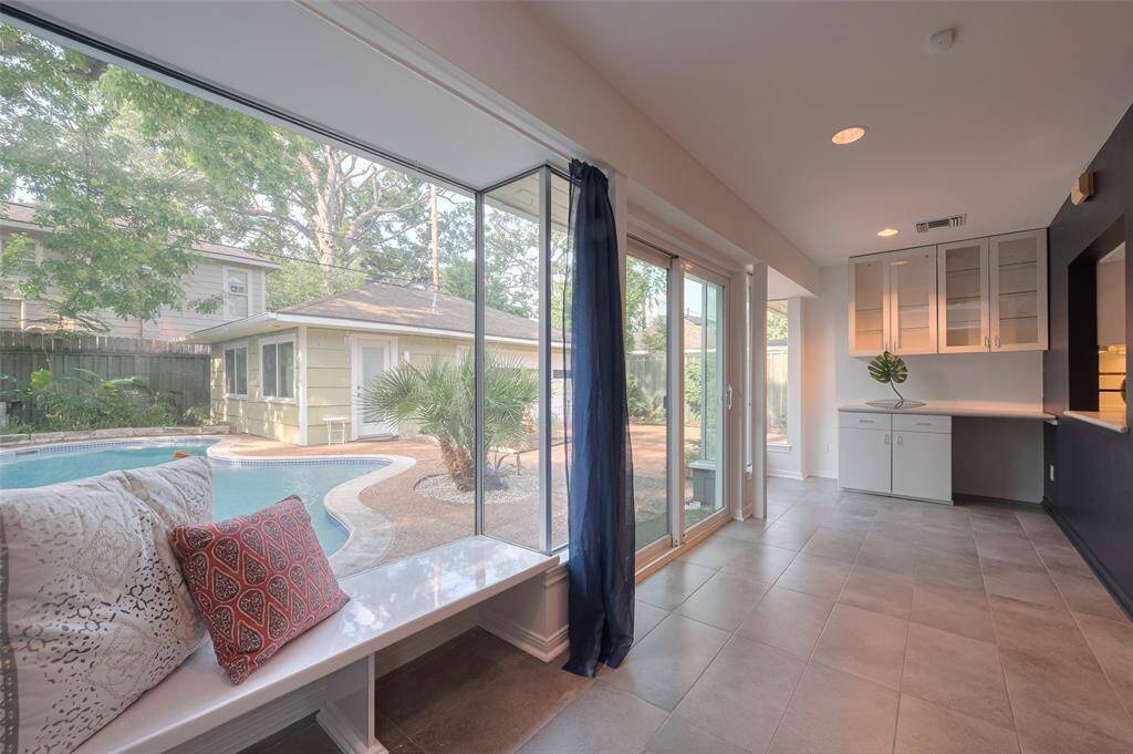 Breakfast room  with large windows overlooking a backyard pool, featuring cozy bench seating with decorative cushions. Ideal for relaxation and enjoying outdoor views.