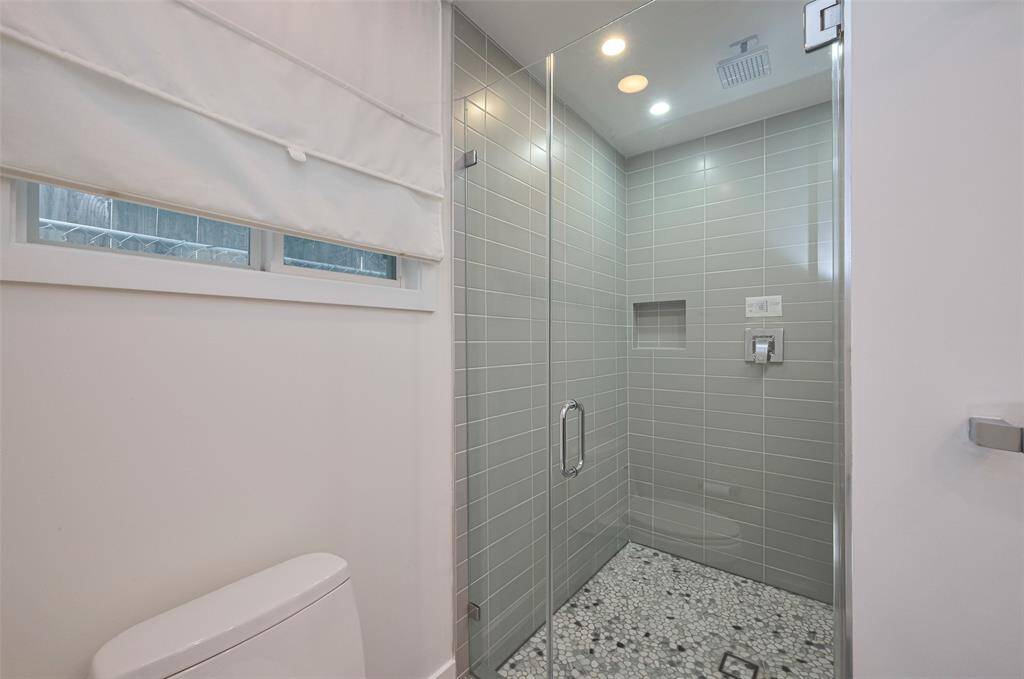 This is a modern bathroom with a sleek marble countertop, under-mount sink, and large mirror. The space features a glass-enclosed shower, minimalist fixtures, and ample lighting, creating a clean and contemporary look.