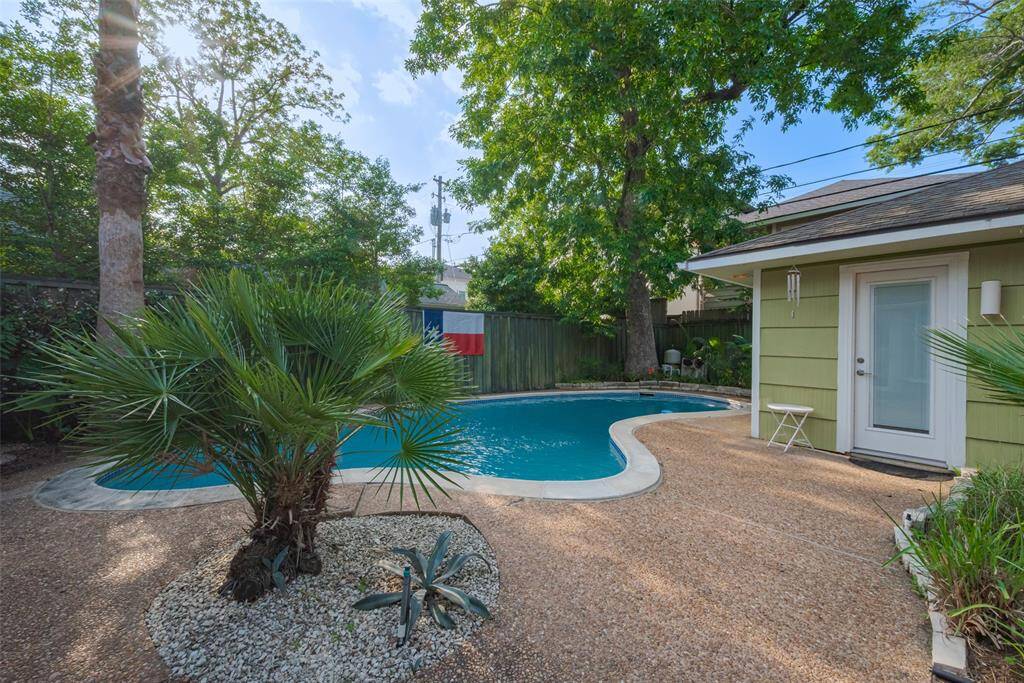 Charming backyard featuring a spacious brick patio, two-car garage, and a lush garden with mature trees. A swimming pool provides a relaxing oasis, perfect for outdoor entertainment and leisure.
