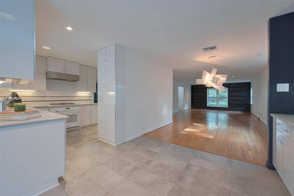 This photo showcases a modern open-plan layout featuring a spacious kitchen with white cabinetry, tiled flooring, and stainless steel appliances.